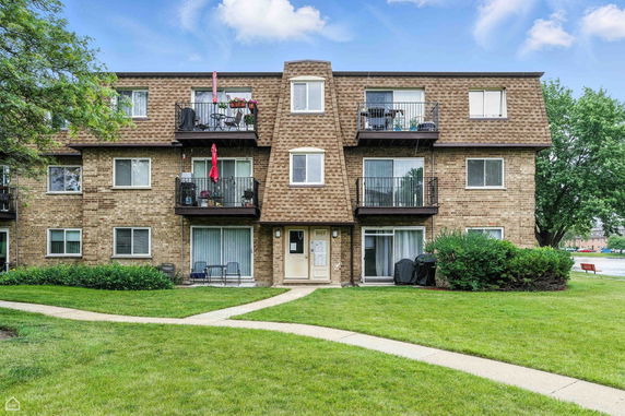 Front view of a three-story brick apartment building with balconies.