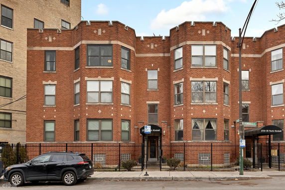 Front view of a brick multi-story building with bay windows.