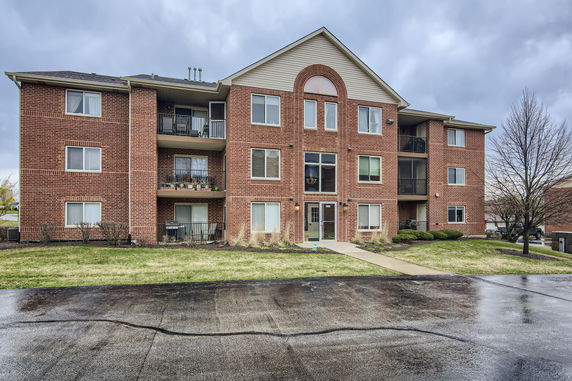 Front view of a three-story brick apartment building with balconies.