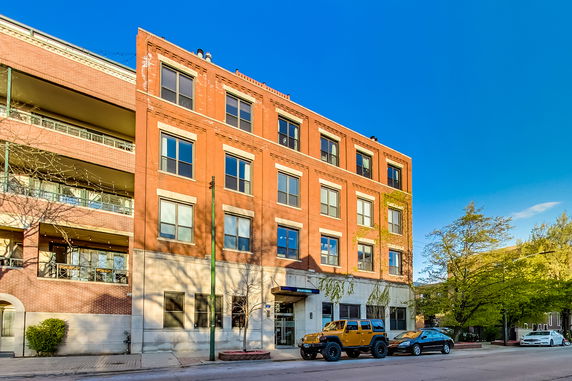 Front view of a four-story brick building with large windows and a street view.