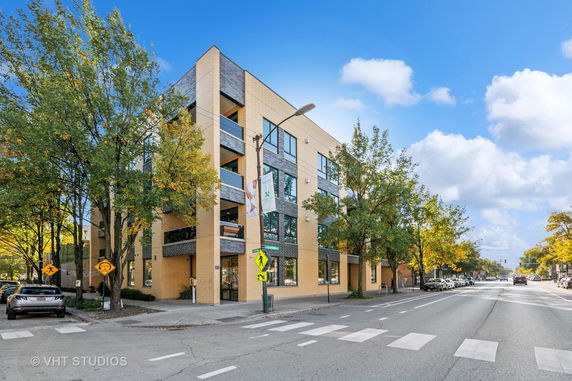 Front view of a modern multi-story building with a light brick exterior and large windows.
