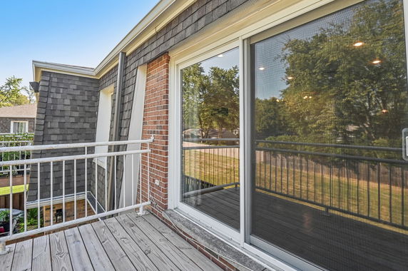 View from a balcony with glass doors reflecting greenery and nearby houses.