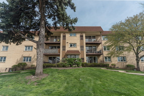 Front view of a multi-story apartment building with balconies and a pitched roof.