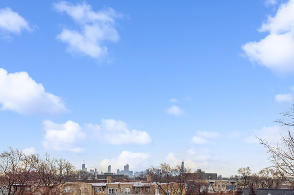 City skyline view with buildings under a blue sky with clouds.