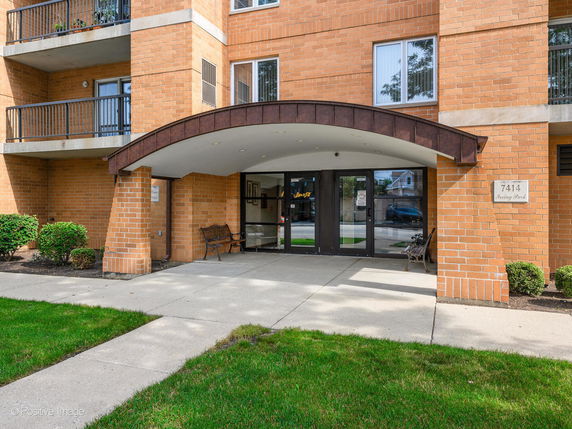 Front view of a brick apartment building entrance with an arched canopy and glass doors.