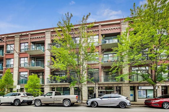 Front view of a multi-story apartment building with balconies and trees.