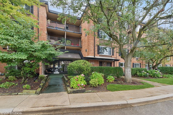 Front view of a multi-story brick building with balconies and a landscaped entrance.