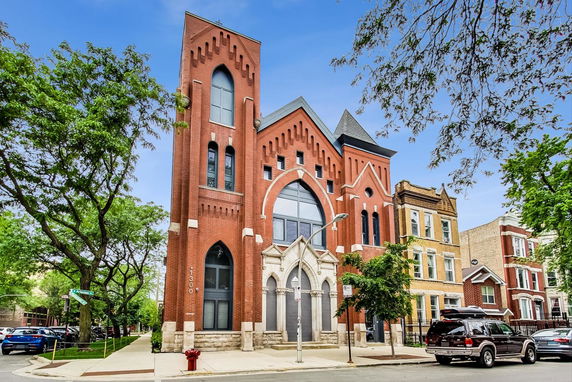 Front view of a red brick multi-story building with arched windows and decorative stone entrance.