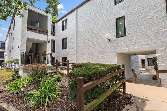 Front view of a white multi-story apartment building with brick exterior and landscaped entrance.