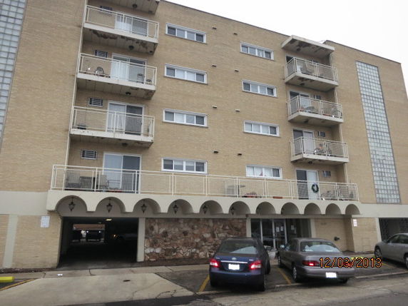 Front view of a multi-story apartment building with balconies and a covered parking area.