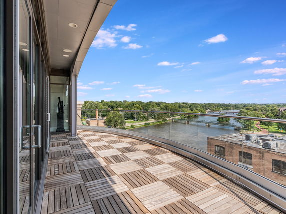 Panoramic view from a balcony with wooden flooring, overlooking a river and green areas.