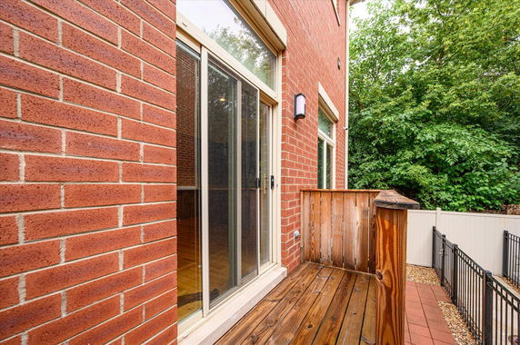 Side view of a brick residential building with sliding glass doors and wooden railing.