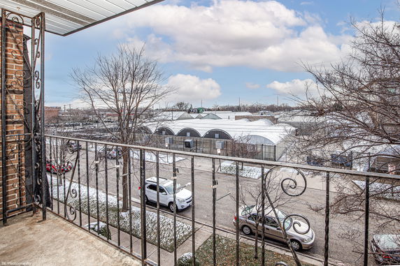 Panoramic view from a balcony showing a street with parked cars and industrial buildings in the distance.
