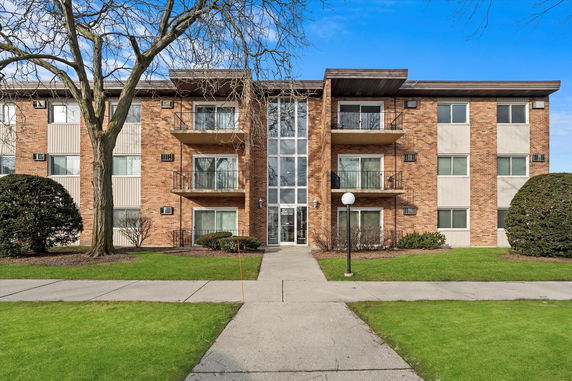 Front view of a three-story brick apartment building with balconies.