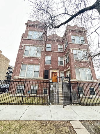 Front view of a multi-story brick building with a gated entrance.