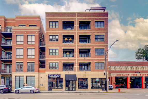 Front view of a multi-story brick apartment building with balconies and ground floor shops.