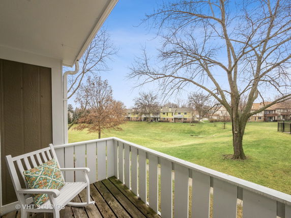 View from a balcony overlooking a grassy area with trees and distant houses.
