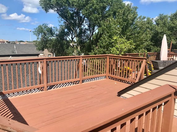 Wooden rooftop deck with railing and trees in the background.