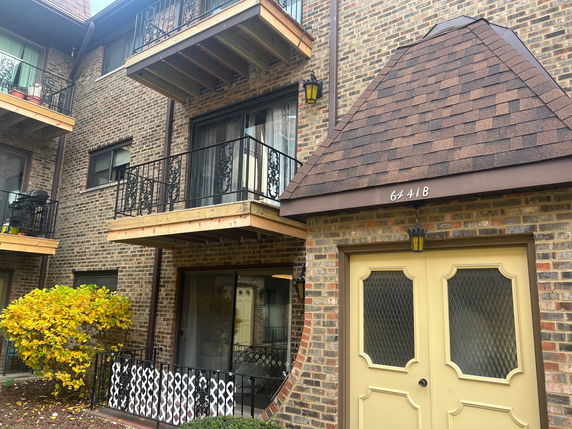 Front view of a multi-story brick building with balconies and a sloped roof entrance.