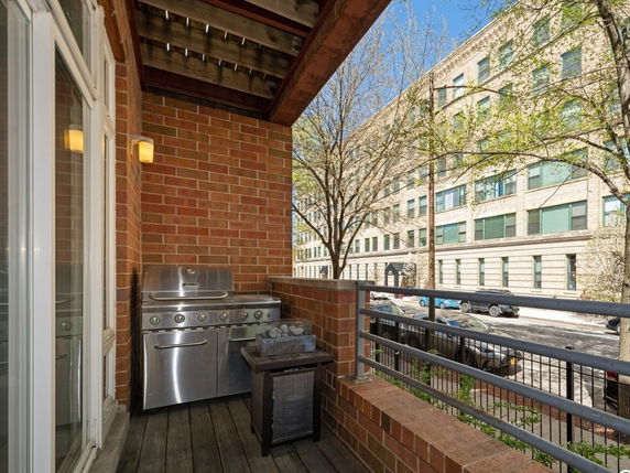 View from a brick balcony with a grill looking towards a street and adjacent building.