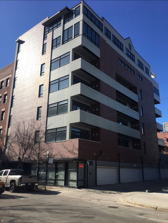 Front view of a multi-story building with balconies and garage doors at street level.