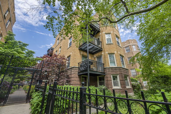 Angle view of a multi-story brick building with balconies and a fenced garden.