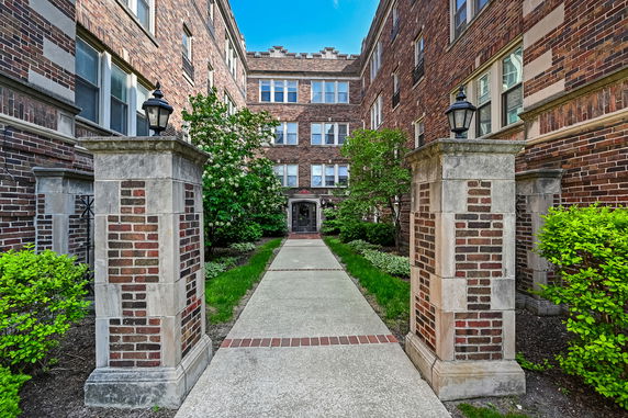Front view of a brick apartment building with a landscaped path leading to the entrance.