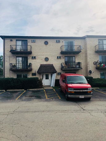 Front view of a three-story apartment building with balconies and a red van parked in front.