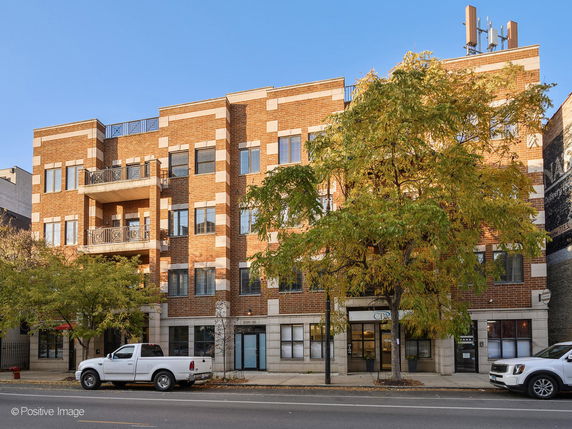 Front view of a multi-story brick building with balconies and street view.