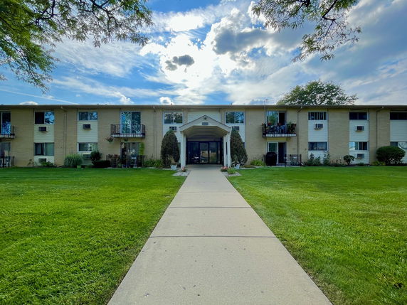 Front view of a multi-story residential building with balconies and a pathway leading to the entrance.