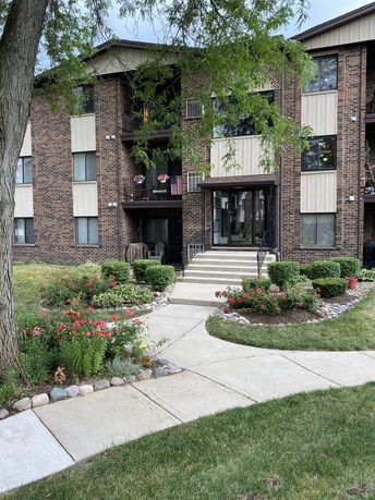 Front view of a multi-story brick building with a landscaped garden and pathway leading to the entrance.
