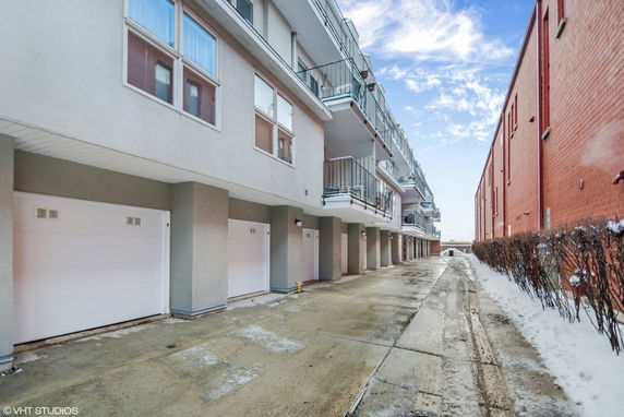 Outdoor parking area beneath a multi-story building with garage doors.