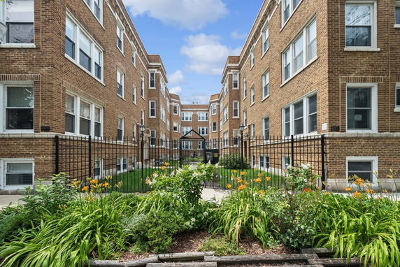 Front view of a multi-story brick apartment building with a gated entrance.
