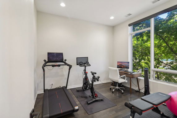 Home gym with exercise equipment, desk, and large window.