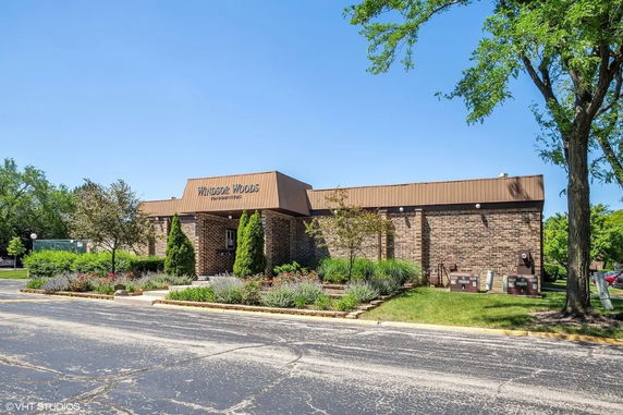 Front view of a single-story brick building with a sign reading 'Windsor Woods Condominiums'.