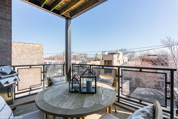 Balcony with a round table and view of surrounding buildings and trees.