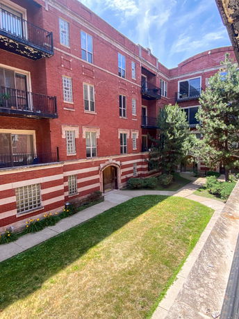 View of a red brick apartment building with balconies and a courtyard.