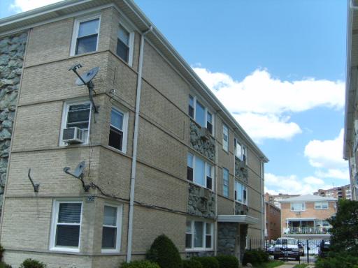 Front view of a multi-story brick building with satellite dishes and window air conditioners.