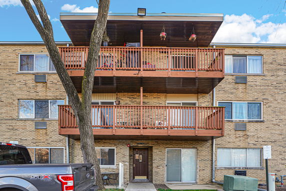Front view of a multi-story brick apartment building with wooden balconies.