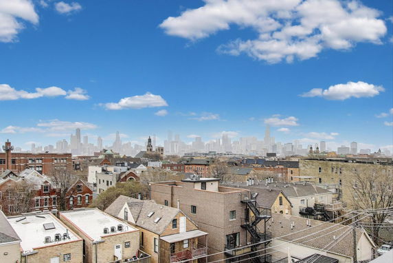 Panoramic view of urban rooftops and a city skyline in the distance under a blue sky with clouds.
