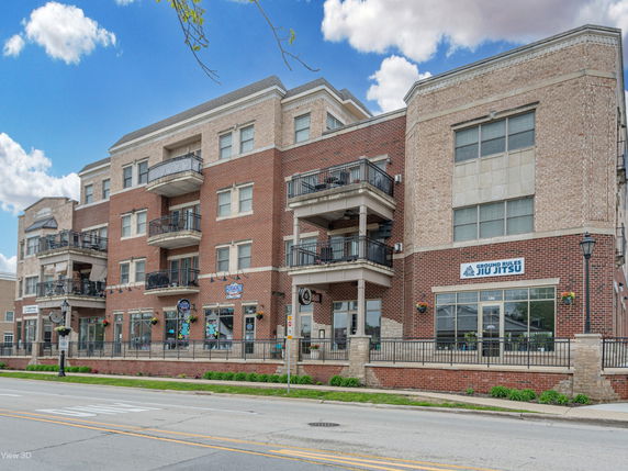 Front view of a multi-story brick building with balconies and commercial spaces on the ground floor.
