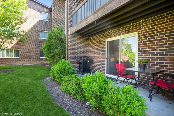 Outdoor view of a brick apartment building with a small patio area including a table, chairs, and a grill.