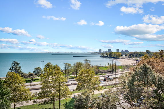 Wide-angle view of a coastal area with a road, trees, and buildings in the distance.