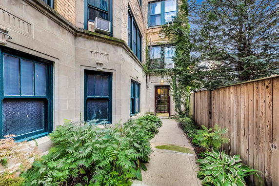 View of a building entrance surrounded by plants with a wooden fence on one side.