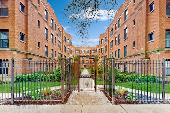 Front view of a brick multi-story apartment building with a gated entrance.