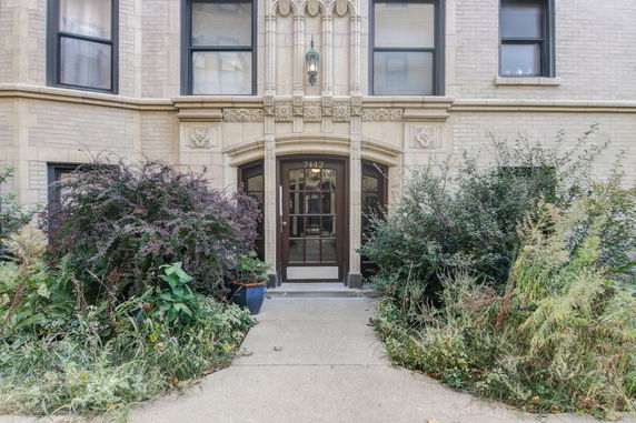 Front view of a building entrance with ornate architectural details and surrounding shrubs.