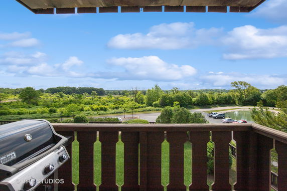 Panoramic view from a balcony overlooking a grassy landscape and a parking area.