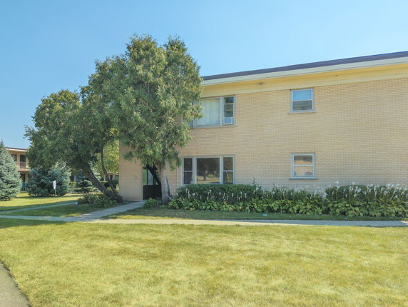 Front view of a two-story brick building with several windows and a surrounding garden area.
