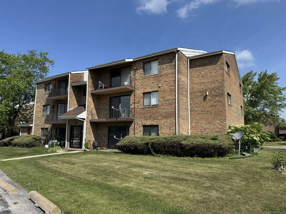 Front view of a three-story brick apartment building with balconies.