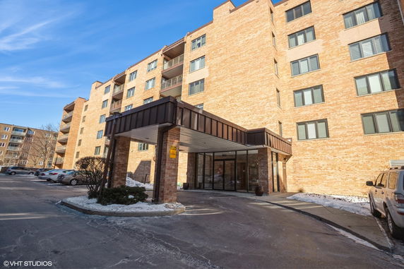 Front view of a multi-story apartment building with a covered entrance and parking area.